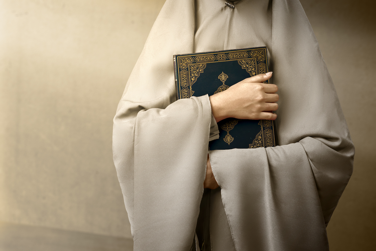 Muslim woman in a veil standing and holding the Quran
