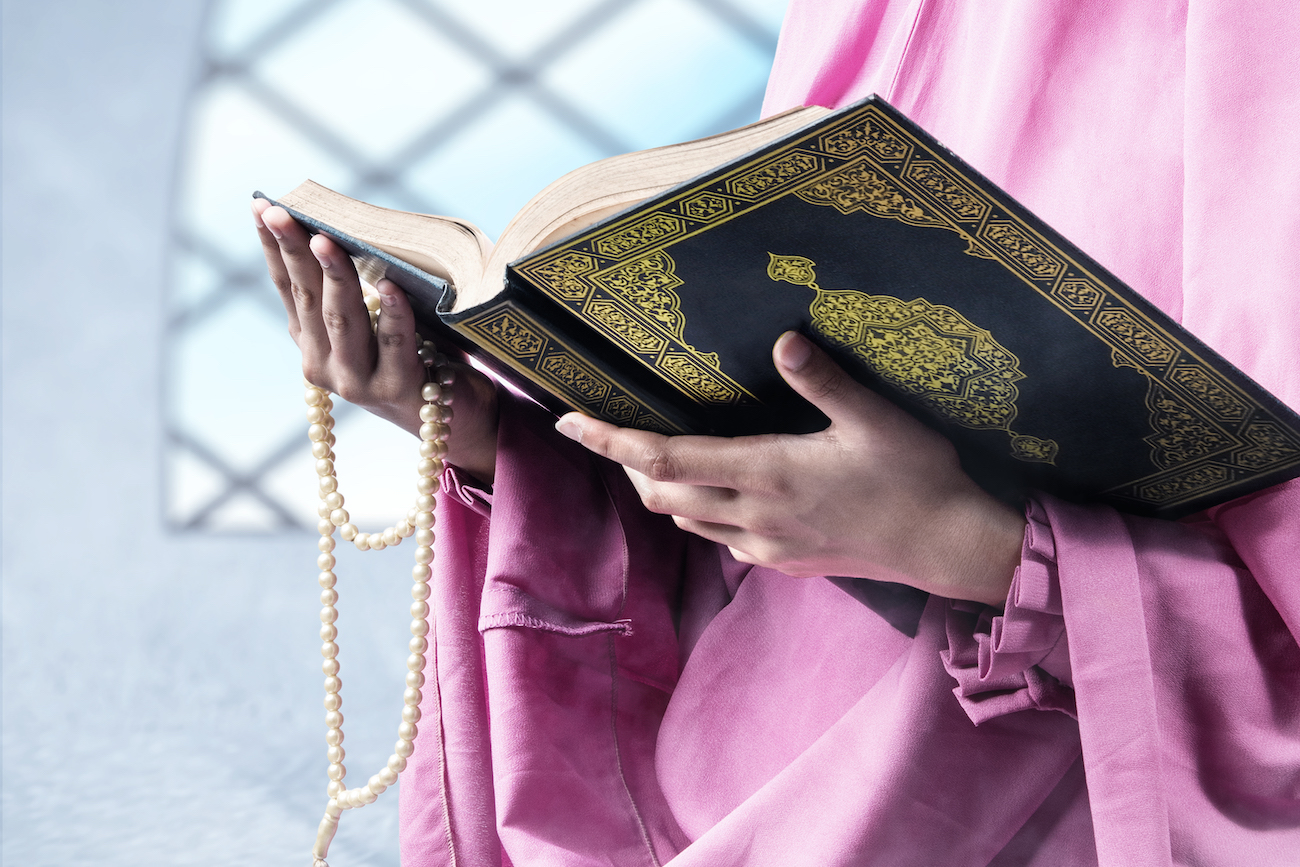 Muslim woman in a veil holding prayer beads and the Quran